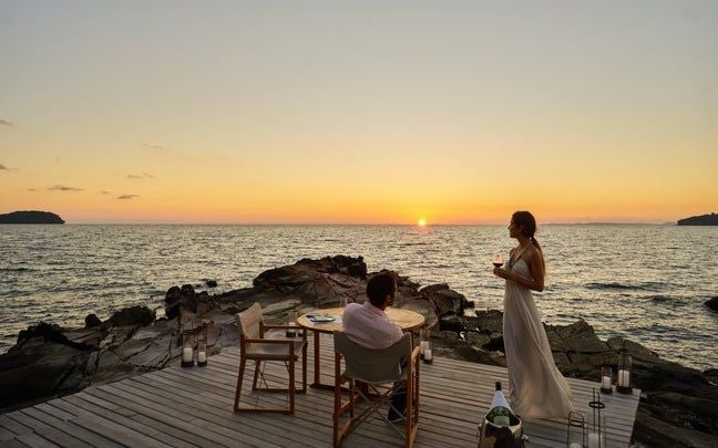 Luxurious overwater villa with infinity pool overlooking turquoise ocean, nestled among tropical greenery at sunset in Cambodia