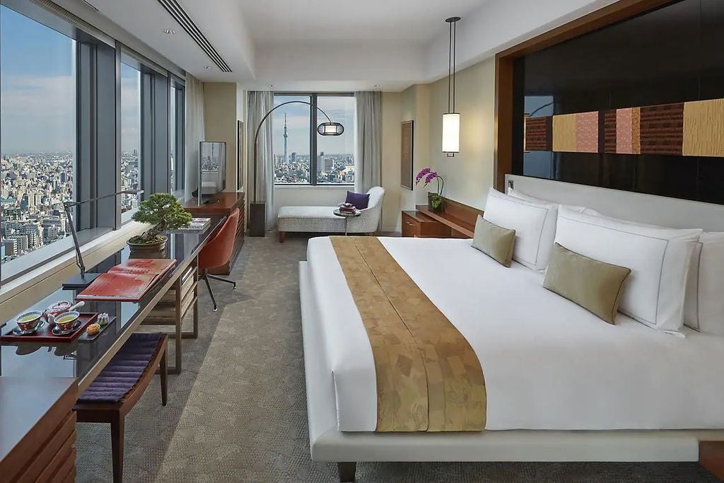 Modern corner room with floor-to-ceiling windows offering Tokyo skyline views, king bed, elegant wood furnishings and gold accents