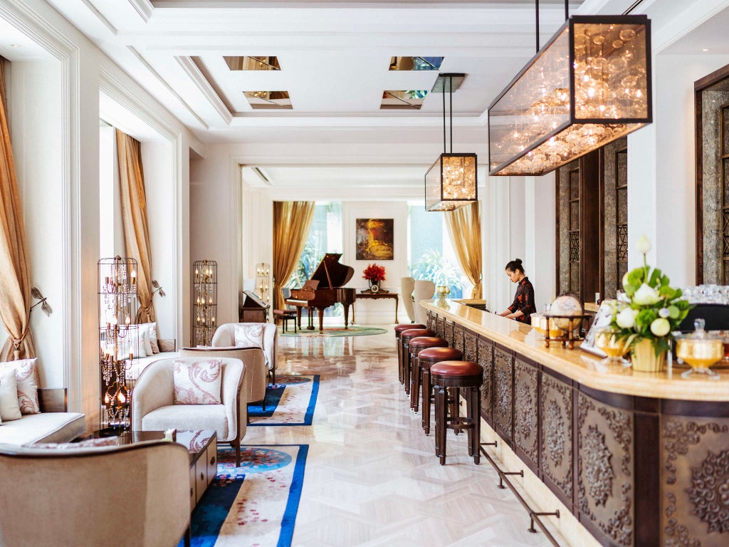 Elegant white colonial-style luxury hotel facade with Art Deco elements, balconies and palm trees in front of Hotel des Arts Saigon