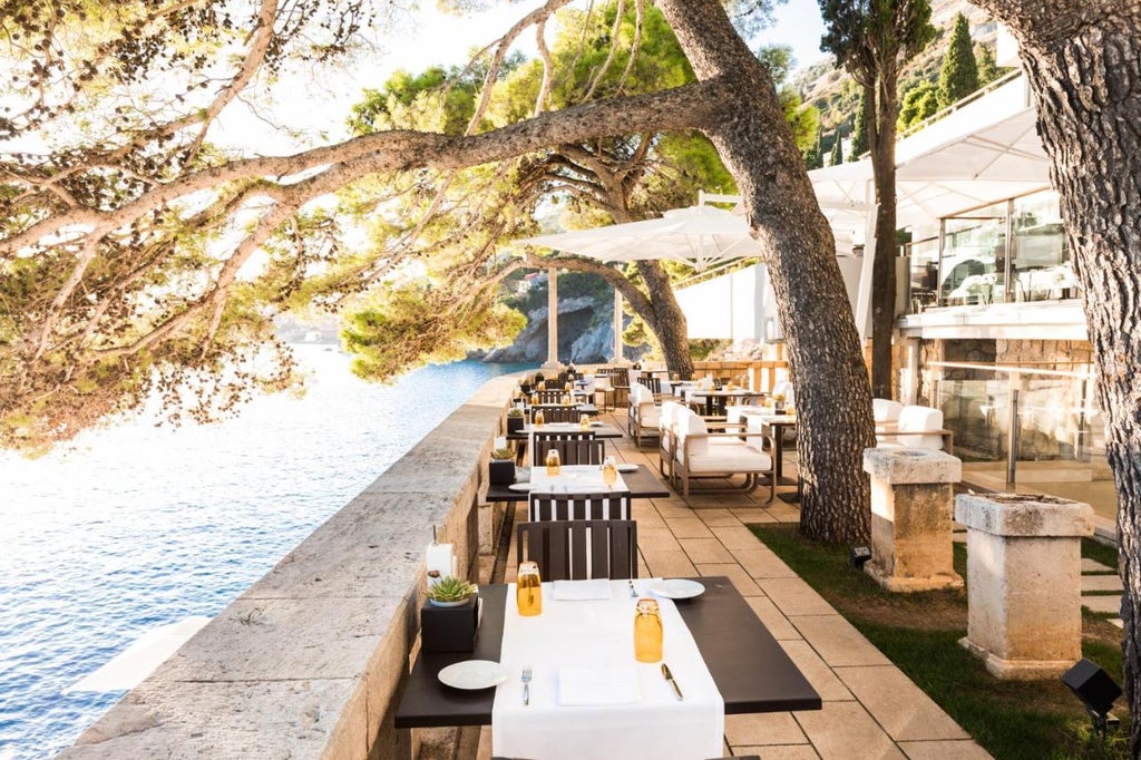 Modern luxury cliffside hotel with glass balconies overlooking the Adriatic Sea, nestled among pine trees with Dubrovnik's old town visible beyond