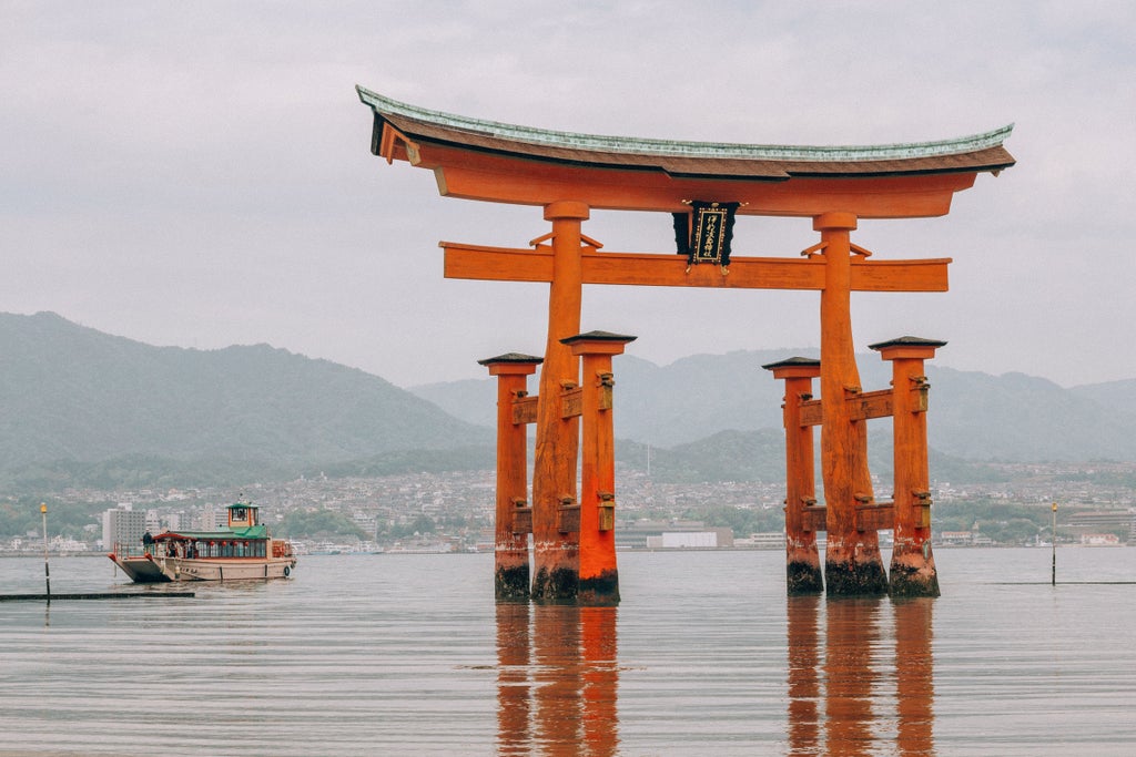 Vermillion torii gate of Itsukushima Shrine stands serenely in water at sunset, with sacred Mount Misen rising behind in Miyajima