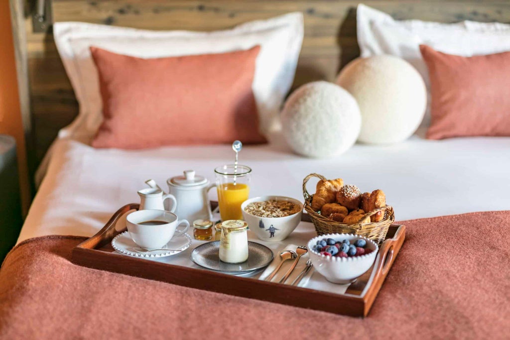 Luxurious alpine prestige room with elegant wooden accents, plush white bedding, and panoramic mountain views at Le Coucou Méribel ski resort in France