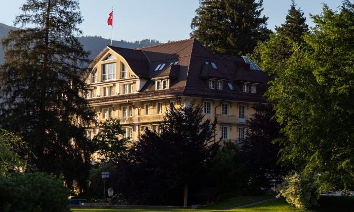 Luxurious Swiss alpine hotel with grand white facade, ornate balconies, and elegant windows overlooking snow-capped mountain landscape at sunset