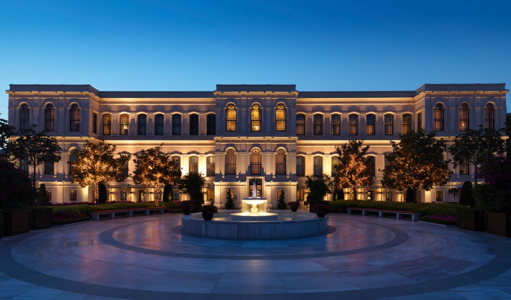 Opulent Ottoman palace-turned-luxury hotel overlooking Bosphorus strait with ornate facade, manicured gardens and waterfront terrace