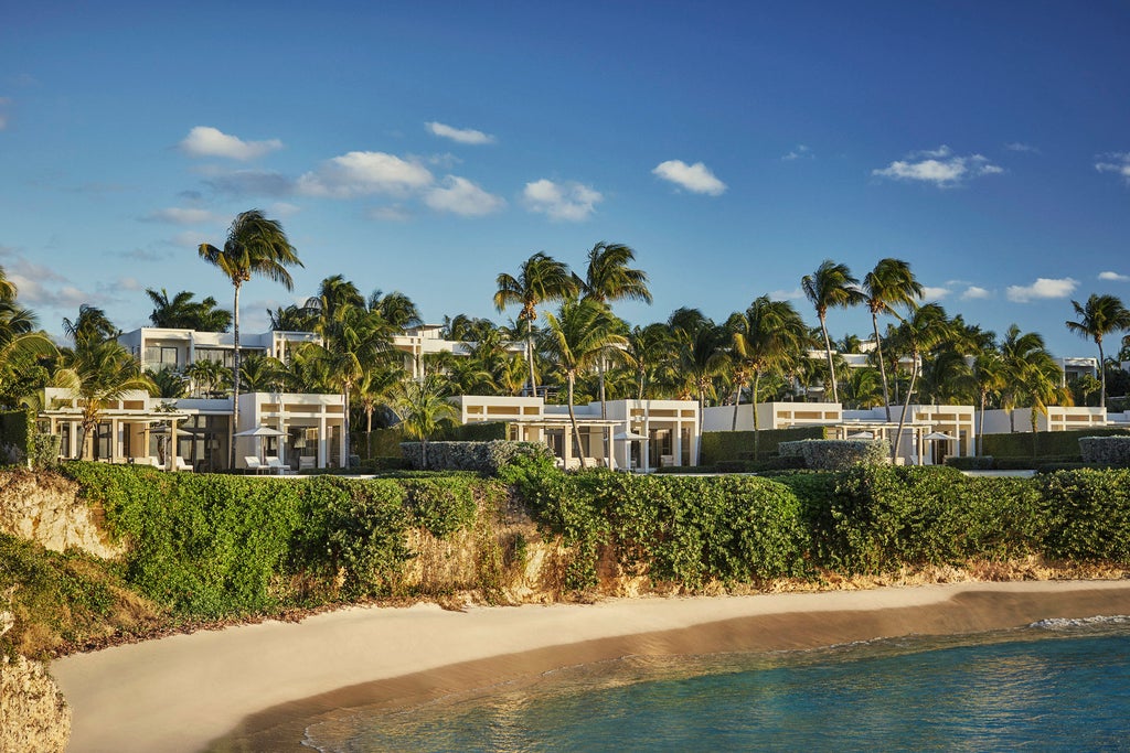 Beachfront infinity pool at Four Seasons Anguilla with sun loungers, white stone pathways and panoramic Caribbean Sea views at sunset