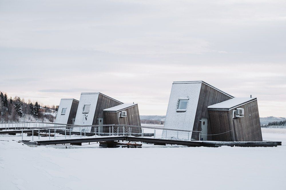 Minimalist wooden water cabin with large windows overlooking snowy landscape, featuring modern Nordic design and suspended architecture at Arctic Bath hotel