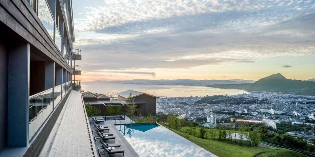 Luxurious modern resort hotel with infinity pools overlooking Beppu city and bay, set against misty mountains at dusk