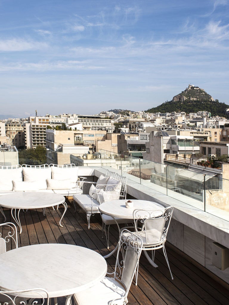 Modern concrete and glass façade of NEW Hotel Athens features geometric patterns and angular balconies glowing warmly at dusk