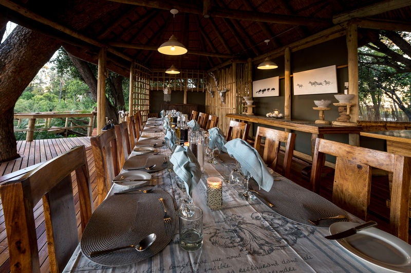 Elevated luxury safari lodge with thatched roof chalets on wooden platforms overlooking Okavango Delta floodplains at sunset