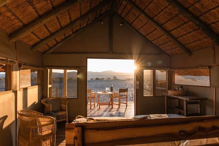 Luxurious canvas and thatch room at Kulala Desert Lodge, featuring rustic elegance with earthy tones, wooden furnishings, and panoramic desert landscape views in Namibia.