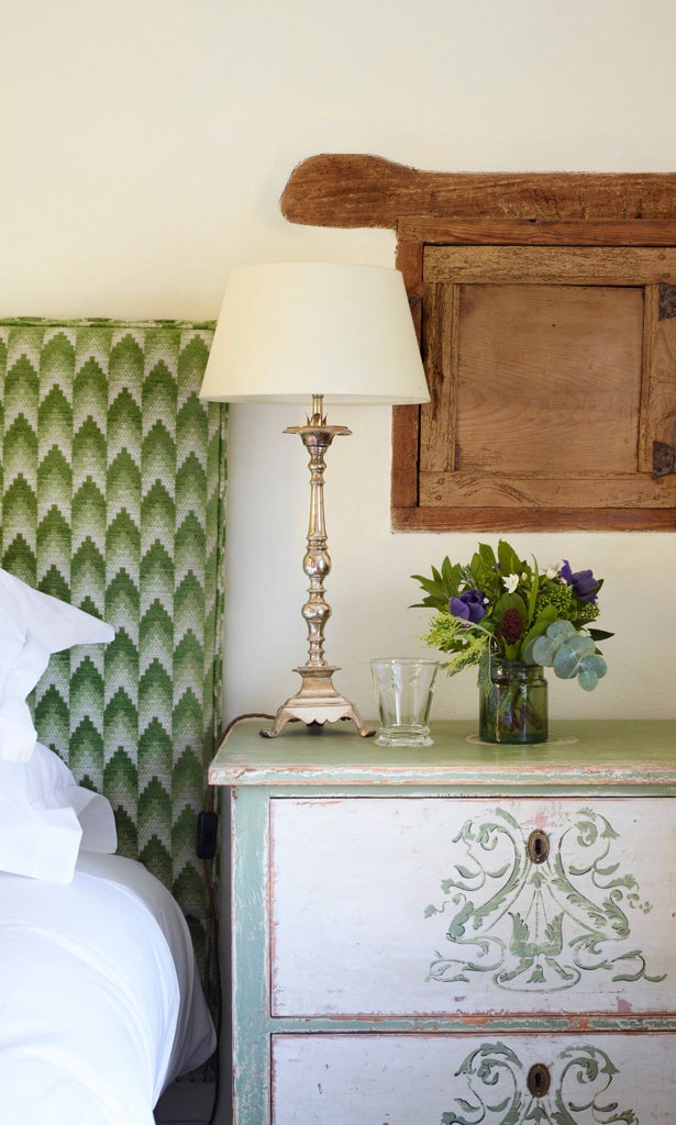 Elegant stone-walled hotel room with rustic wooden furniture, soft linen bedding, and warm ambient lighting creating a cozy, luxurious countryside retreat