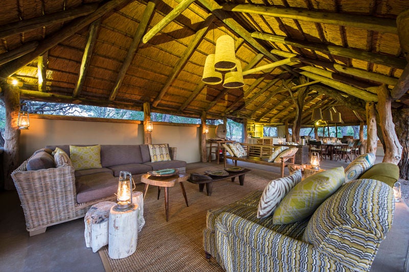 Elevated safari lodge overlooking Botswanan plains, featuring thatched-roof pavilions, private decks, and infinity pool amid acacia trees