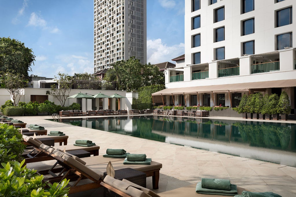 Elegant Thai-style hotel entrance with reflecting pool, ornate teak pavilions, and lush tropical gardens under evening sky at The Sukhothai Bangkok