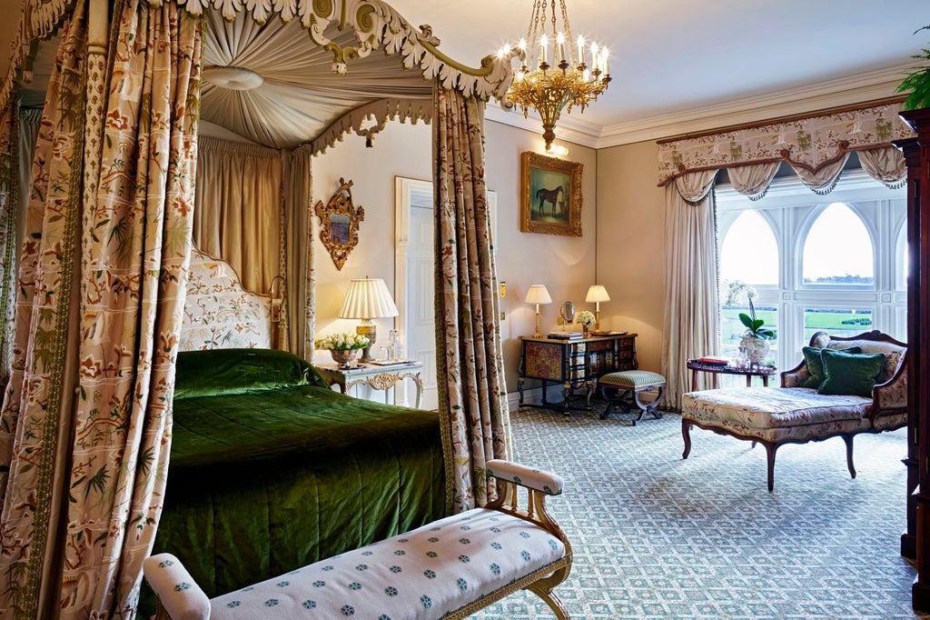 Luxurious hotel suite with antique furnishings, crystal chandelier, high ceilings, and ornate drapes framing large windows overlooking castle grounds