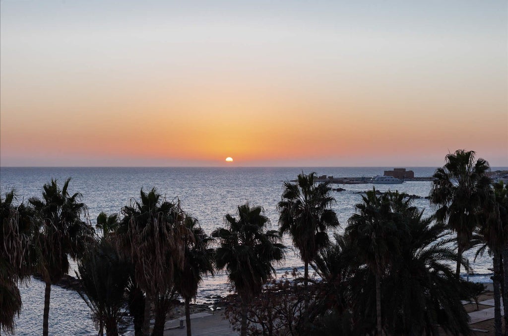 Luxurious seafront resort with white Mediterranean architecture, azure pool, and palm trees overlooking stunning Cyprus coastline at sunset