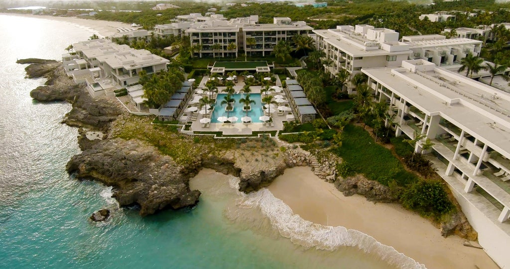 Oceanfront infinity pool overlooking Caribbean Sea at Four Seasons Anguilla, with luxurious white loungers and swaying palm trees