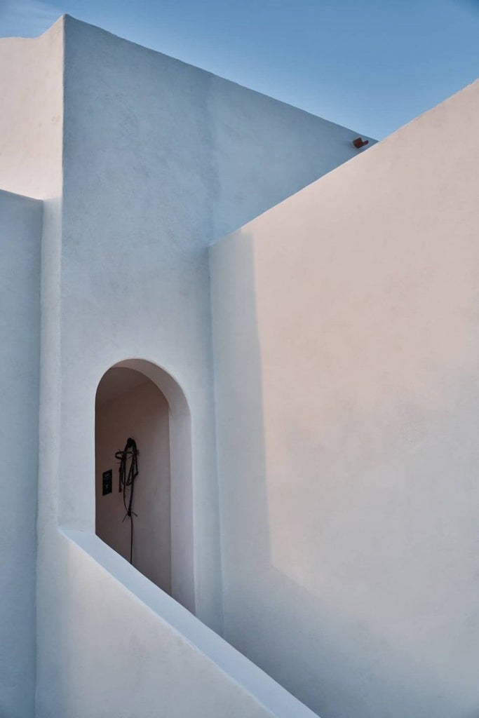 White stone luxury suite with private oval pool, curved archways and stairs overlooking Santorini's caldera at sunset