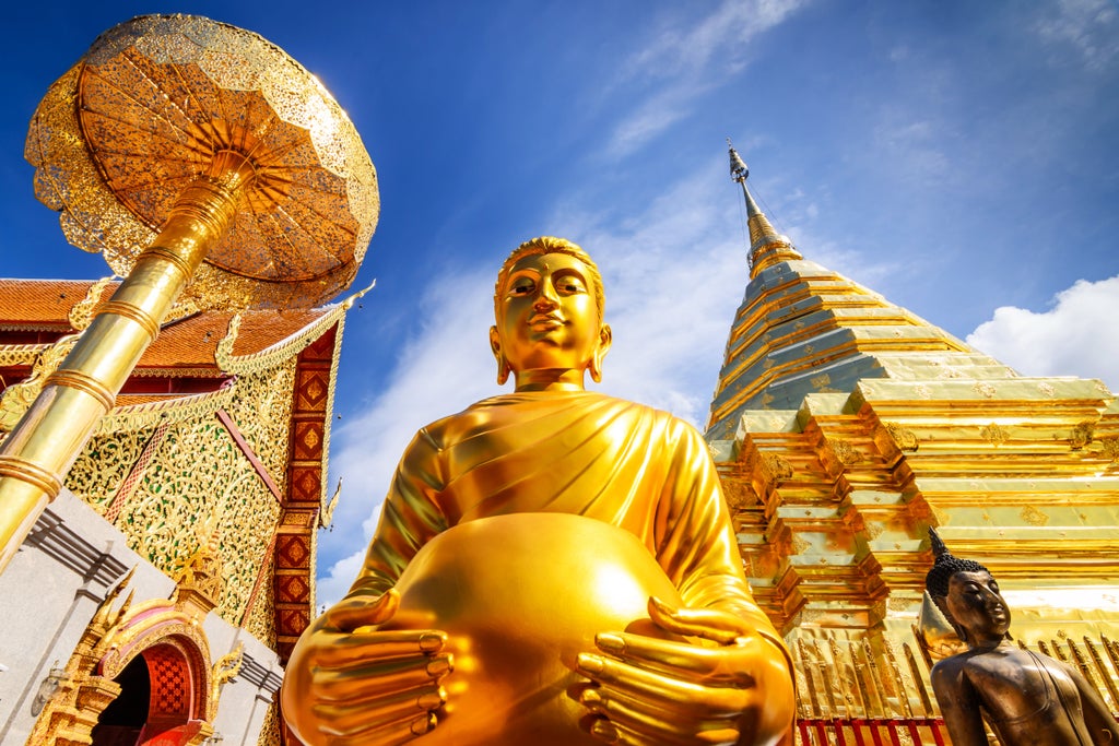 Gold-adorned temple gateway in Bangkok featuring ornate Thai architectural details, red columns and traditional roof against blue sky