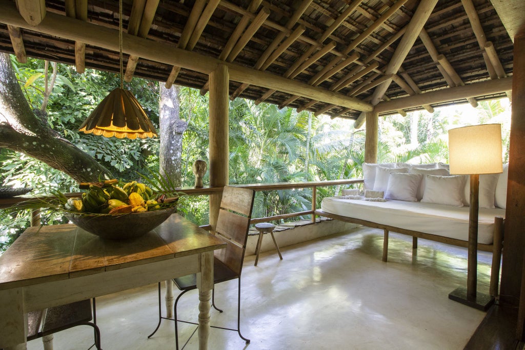 Lush tropical garden surrounds elegant rustic wooden villa with vibrant colors, traditional Brazilian architecture, and luxurious outdoor spa setting in Trancoso