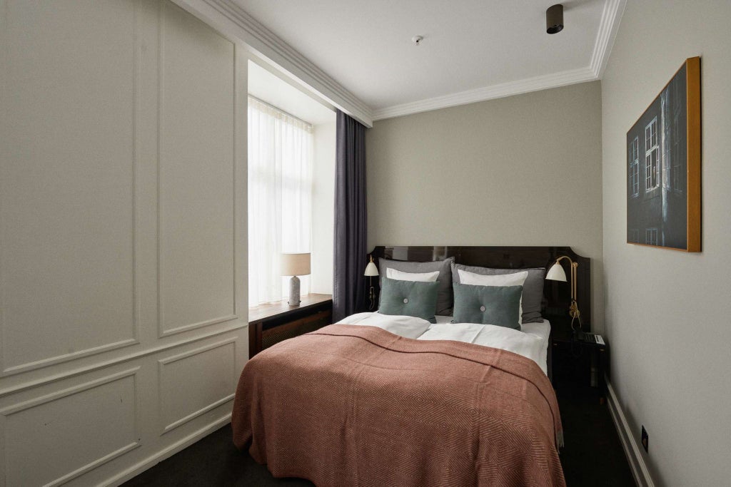 Elegant small deluxe hotel room with minimalist Danish design, crisp white linens, warm wood accents, and soft natural lighting in Copenhagen