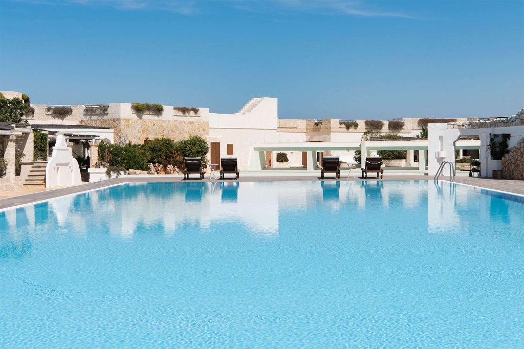 Elegant coastal hotel with blue-tiled pool overlooking azure Adriatic Sea, luxurious Mediterranean architecture nestled among lush Italian landscaping