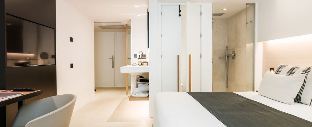 Elegant modern double room with minimalist design, white linens, wooden headboard, and soft ambient lighting in boutique Spanish hotel