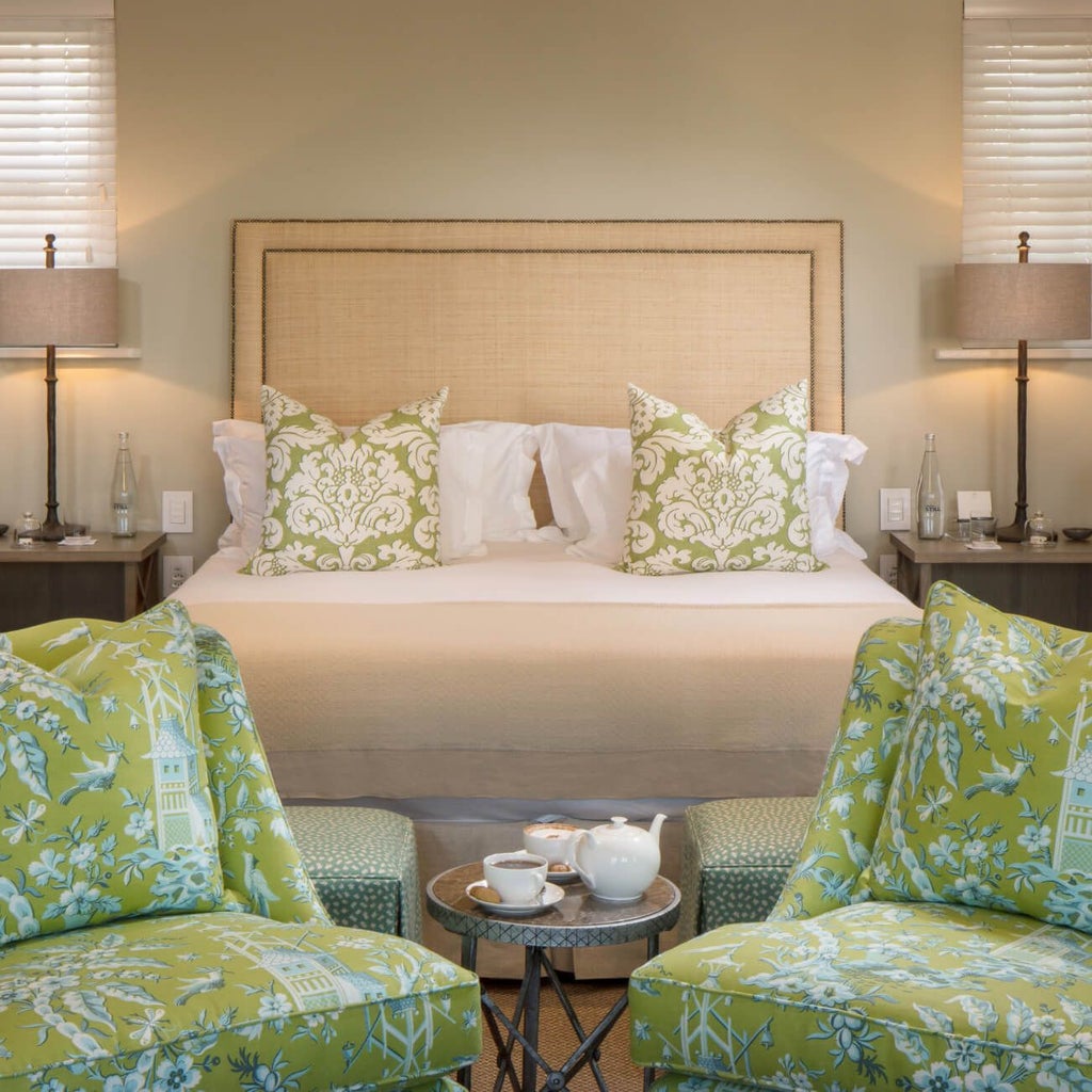 Luxurious pool suite with crisp white linens, elegant wooden furniture, and large windows overlooking a lush garden at Le Quartier Français in Franschhoek, South Africa