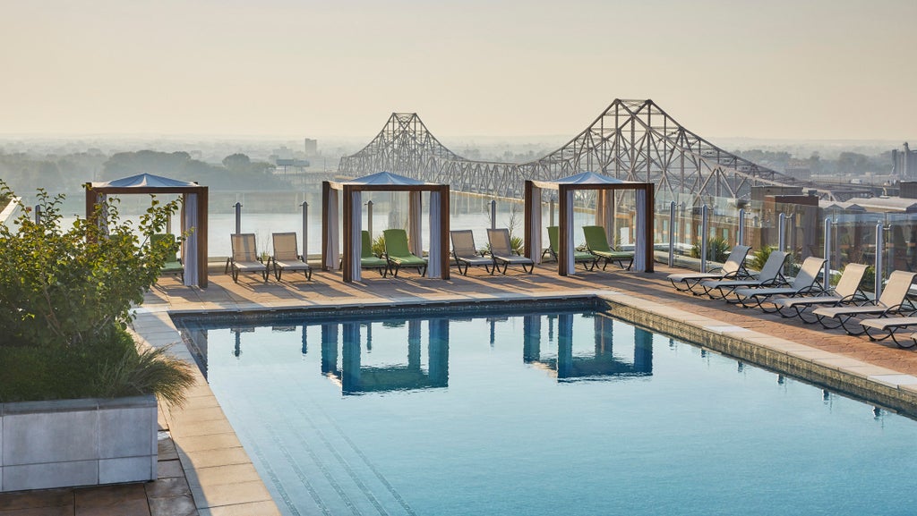 Modern high-rise Four Seasons hotel with glass facade reflects city lights at dusk, featuring illuminated rooftop pool and St. Louis Arch view