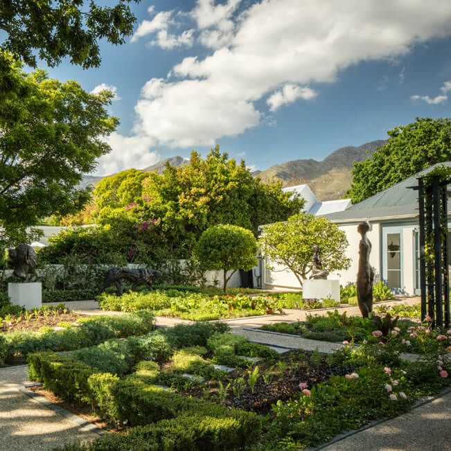 Elegant luxury hotel entrance with stone archway, manicured gardens and terracotta walls beneath South African mountains at sunset