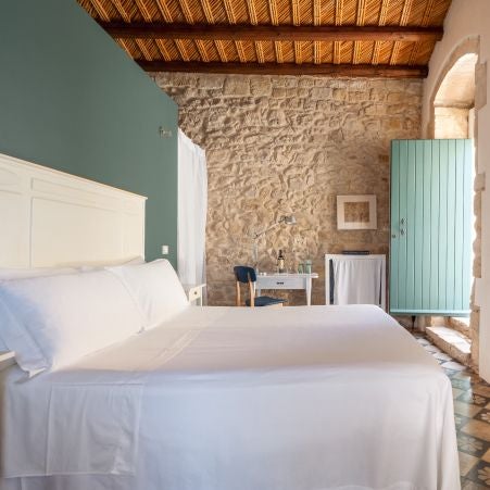 Elegant rustic Italian hotel room with exposed stone walls, minimalist wooden furnishings, soft natural light, and warm terracotta accents in Scenset's Casa Talía suite