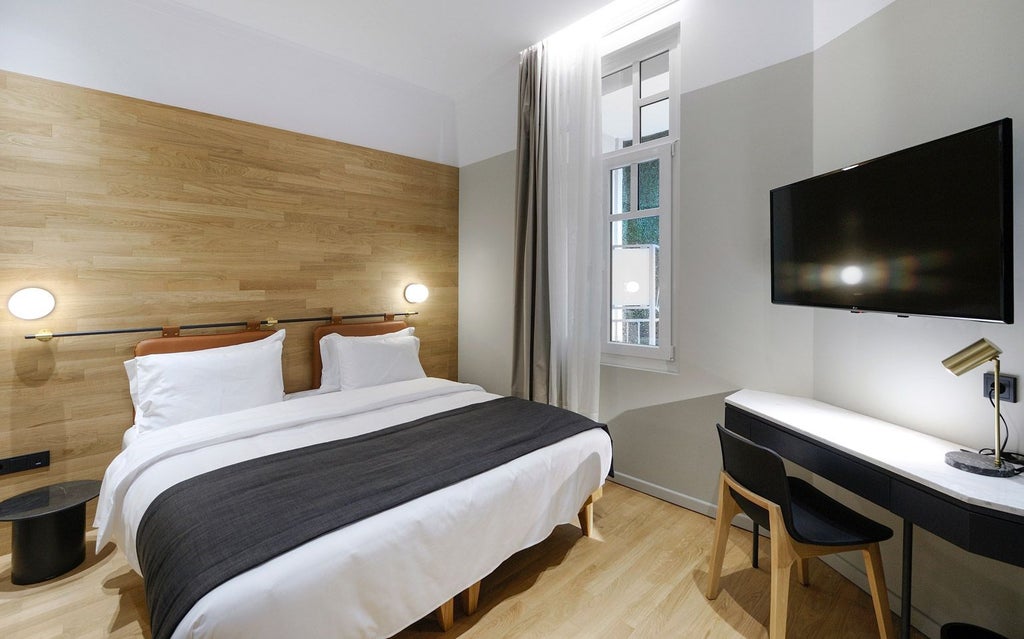 Minimalist hotel room with sleek gray furniture, crisp white linens, large window overlooking urban scenset skyline in Thessaloniki, Greece