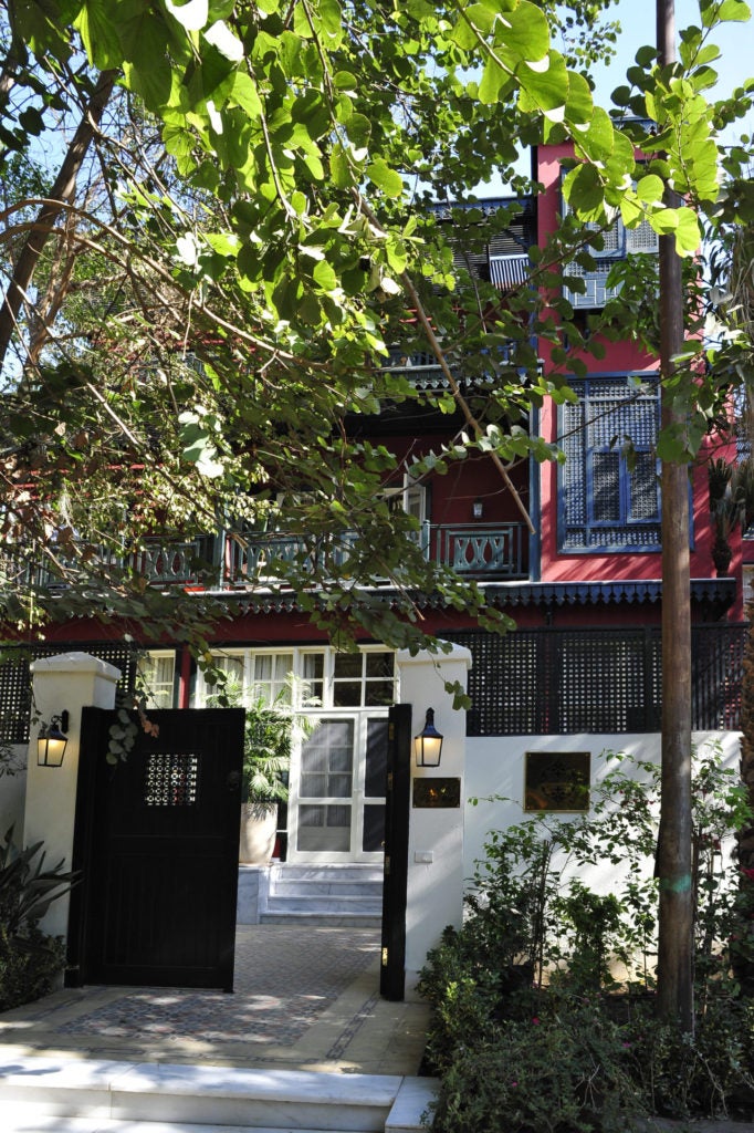 Historic Egyptian boutique hotel exterior with elegant arched windows, palm trees, and manicured garden set in classic Maadi architecture