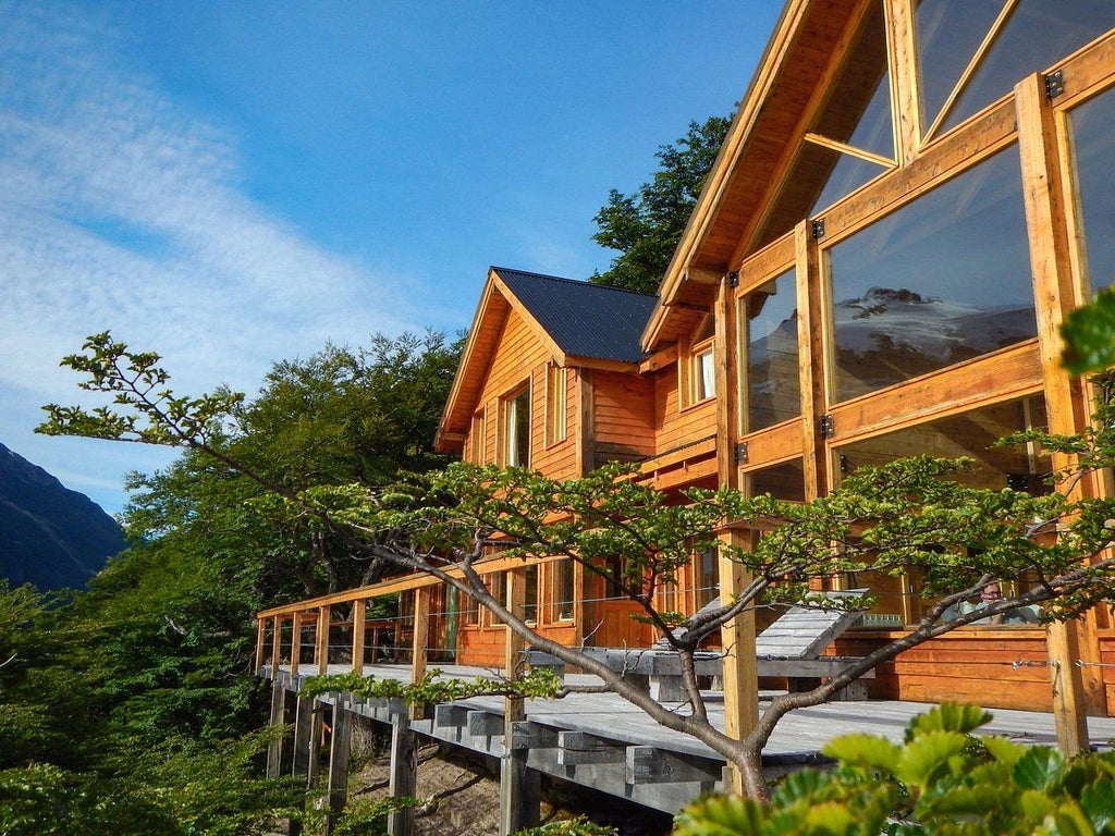 Luxurious lodge nestled against snow-capped Andes mountains, with rustic wood exterior reflecting in pristine Patagonian lake waters