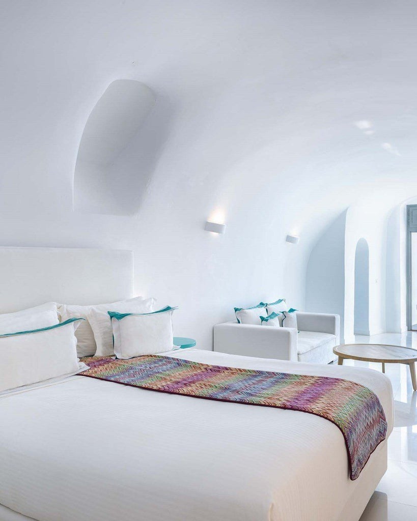 Elegant white-washed senior suite with private terrace overlooking Aegean Sea, luxurious minimalist design, blue-domed architecture in Santorini