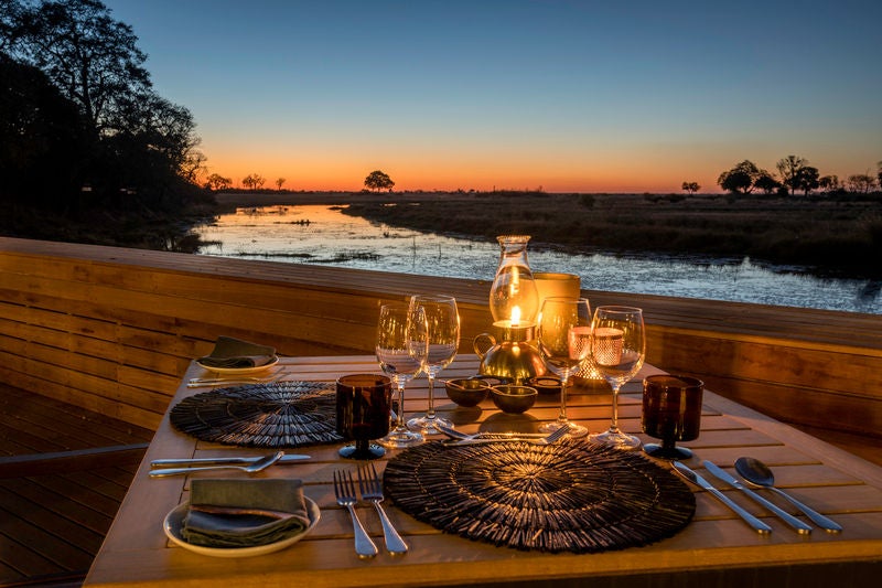 Elegant safari lodge deck overlooking Botswana river, with plush outdoor seating and plunge pool surrounded by wild savanna