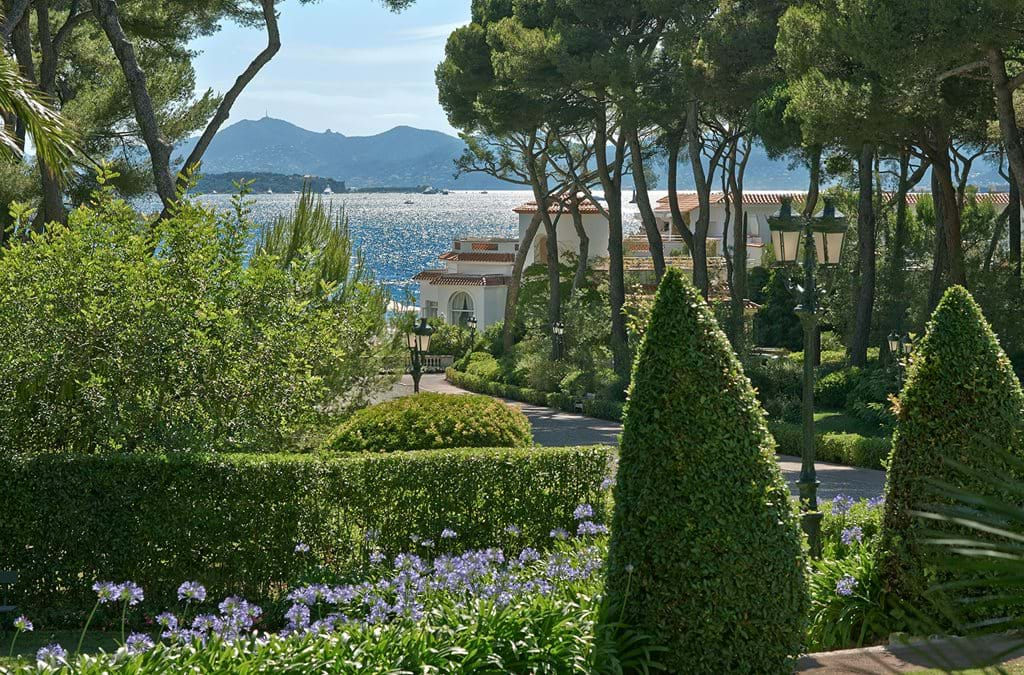 Elegant Mediterranean hotel with white facade and red terracotta roof nestled on rocky cliffs overlooking French Riviera's azure waters