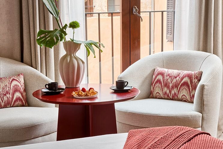 Elegant Spanish hotel room with white linens, warm wood furnishings, rustic stone wall, and soft natural light highlighting classic Mediterranean design.