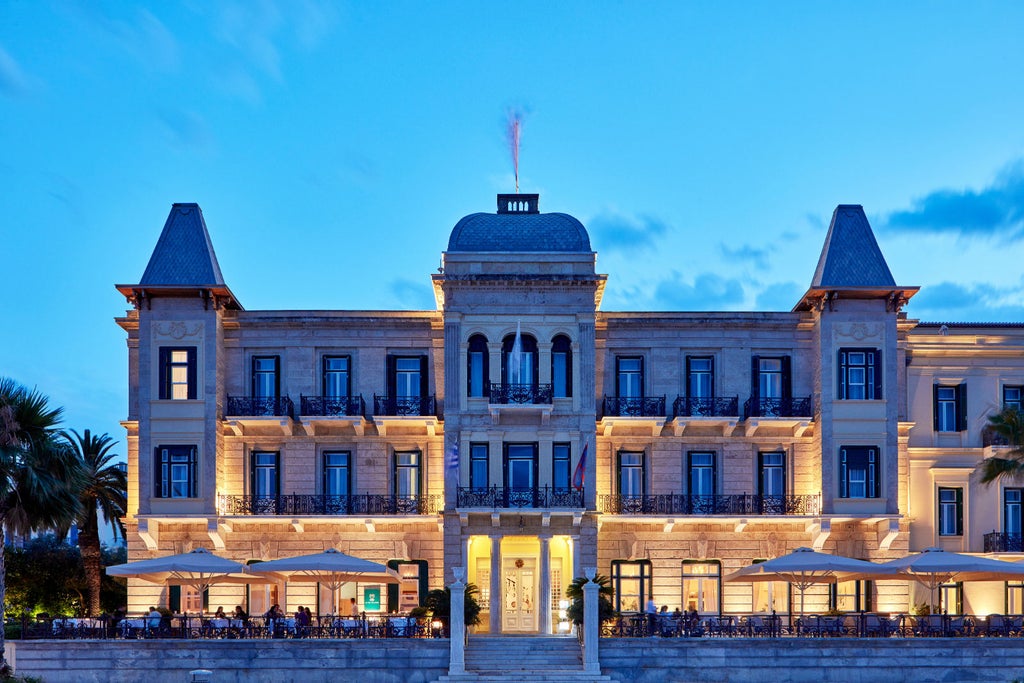 Elegant white neoclassical seaside hotel with grand pillars, ornate balconies, and manicured gardens overlooking the Mediterranean