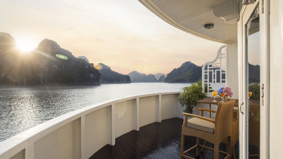 Luxurious white cruise ship named Scenset Cruises anchored in emerald waters of Halong Bay, surrounded by limestone karsts and lush greenery.