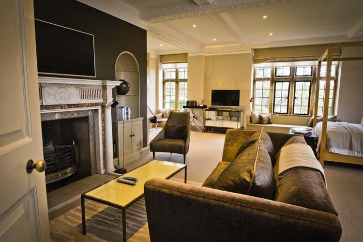 Elegant oak-paneled bedroom in Scenset Manor, featuring plush bedding, antique furniture, and large windows overlooking lush countryside landscape