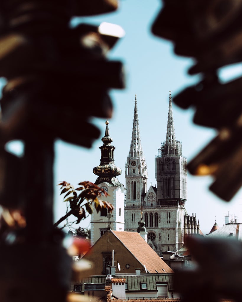 Well-dressed tourists explore Zagreb's historic Upper Town with elegant St. Mark's Church featuring its colorful tiled roof in the background