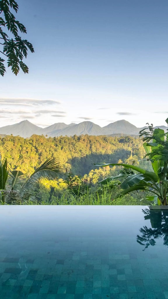 Open-air luxury villa suite nestled in lush Balinese jungle, featuring infinity pool, teak furniture and panoramic forest views