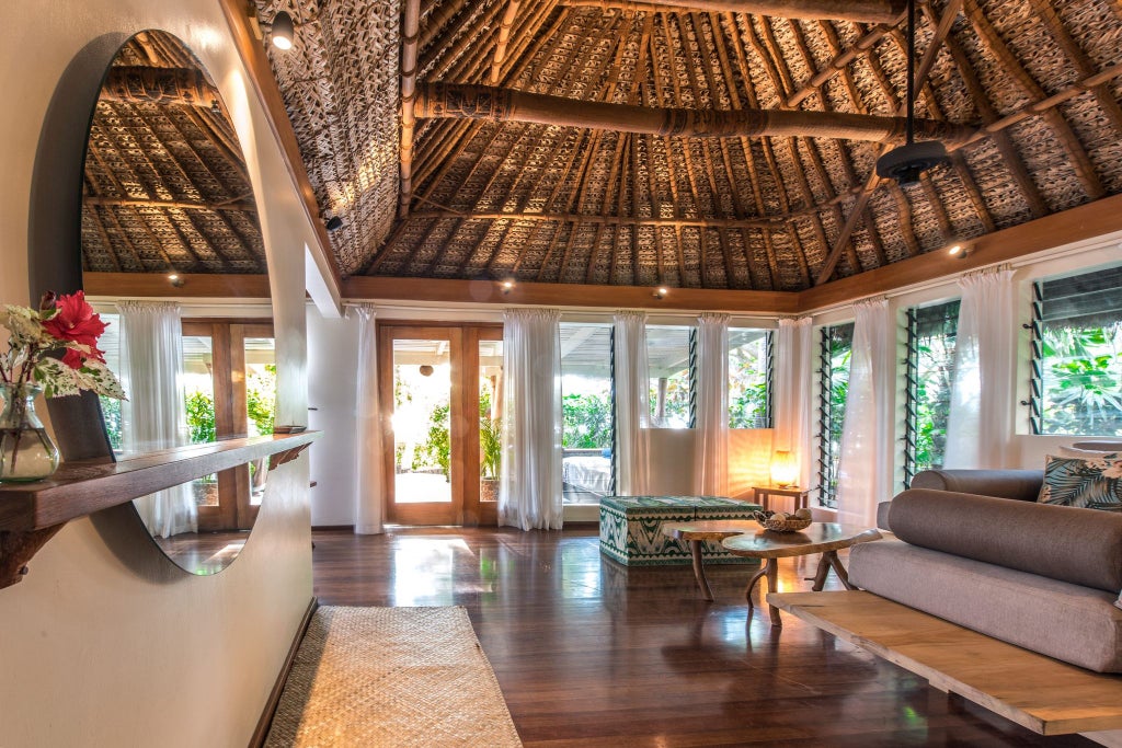 Spacious beachfront villa with open-air design, white linens, tropical wooden decor, panoramic ocean view, and lush Fijian landscape in background