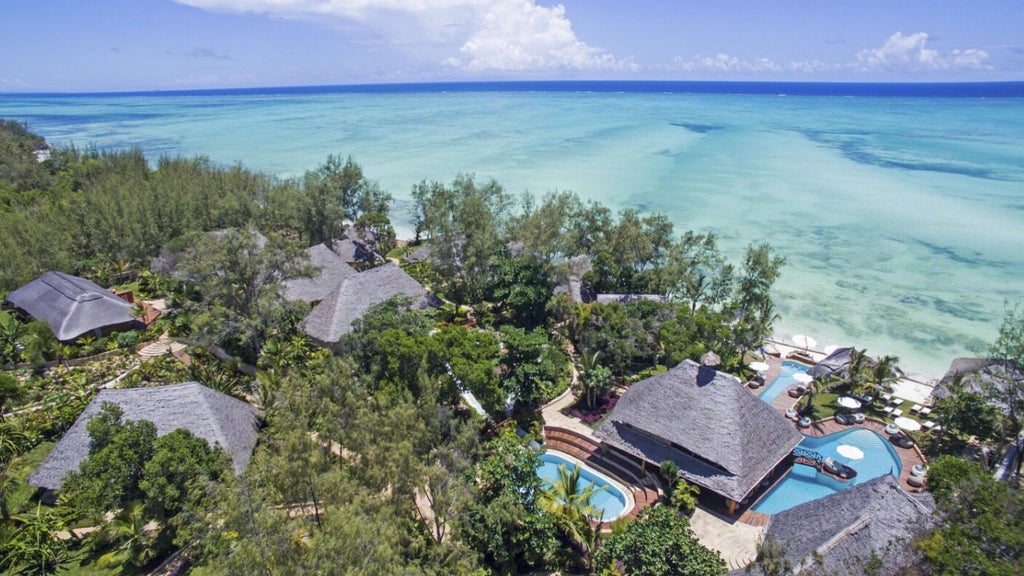 Luxurious oceanfront villa with private infinity pool, white sand beach, and swaying palm trees at Tulia Zanzibar resort at sunset