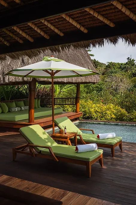 Luxurious open-air villa with traditional thatched roof overlooking lush tropical landscape at NIHI Sumba resort in Indonesia, featuring elegant wooden furnishings