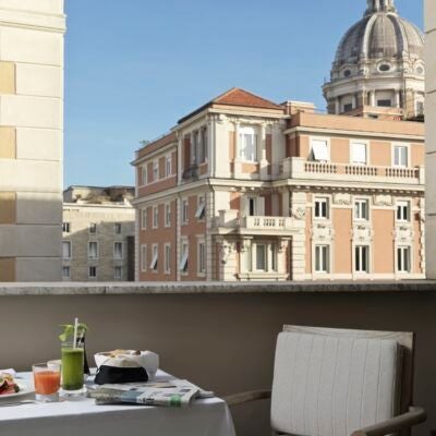 Elegant interior of luxurious Roma hotel with marble floors, designer furniture, and sophisticated cream and gold color palette overlooking historic Italian cityscape