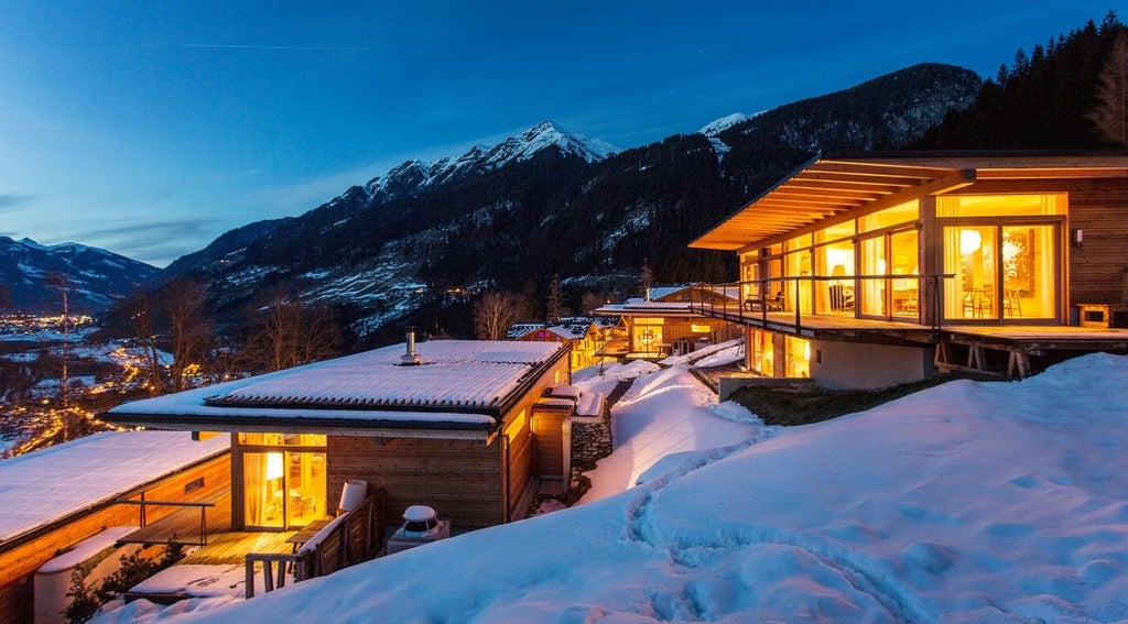 Modern alpine hotel exterior with floor-to-ceiling windows, sleek balconies, and mountain views in a tranquil Austrian setting