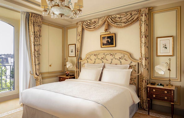 Elegant Parisian hotel room with crystal chandelier, Louis XV furniture, gold-framed mirror, pastel silk walls and plush queen bed