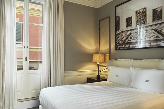 Elegant Italian hotel room with cream walls, plush white bedding, designer furniture, and soft natural light streaming through large windows