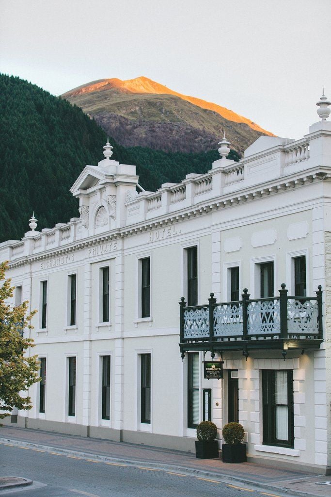 Historic stone-facade luxury hotel with elegant arched windows, overlooking Lake Wakatipu and mountains in Queenstown, New Zealand